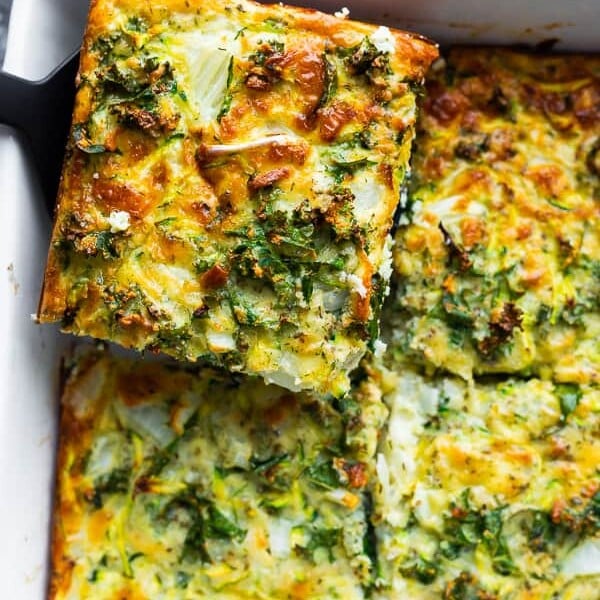 overhead shot of a slice of herb zucchini and kale egg bake being lifted out of the pan by a spatula