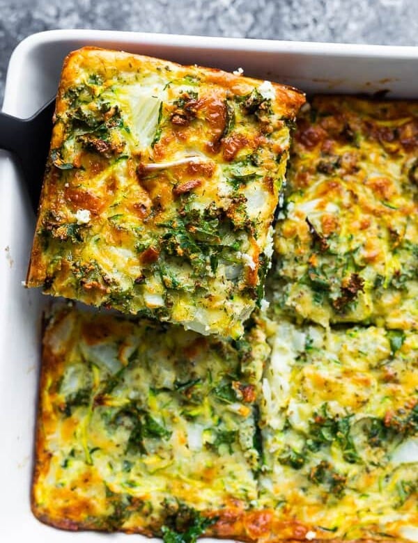 overhead shot of a slice of herb zucchini and kale egg bake being lifted out of the pan by a spatula