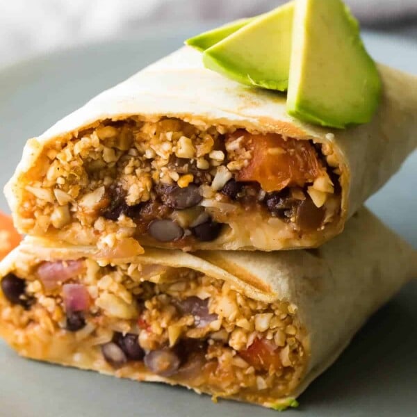 cauliflower rice black bean burrito cut in half and stacked on a plate with avocado slices