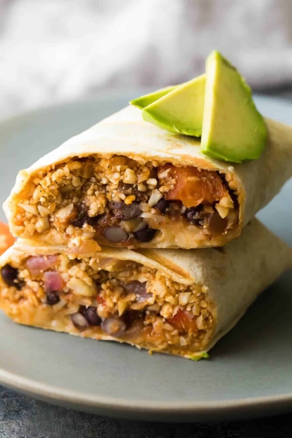 cauliflower rice black bean burrito cut in half and stacked on a plate with avocado slices