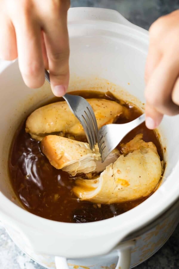 small slow cooker with two forks shredding chicken