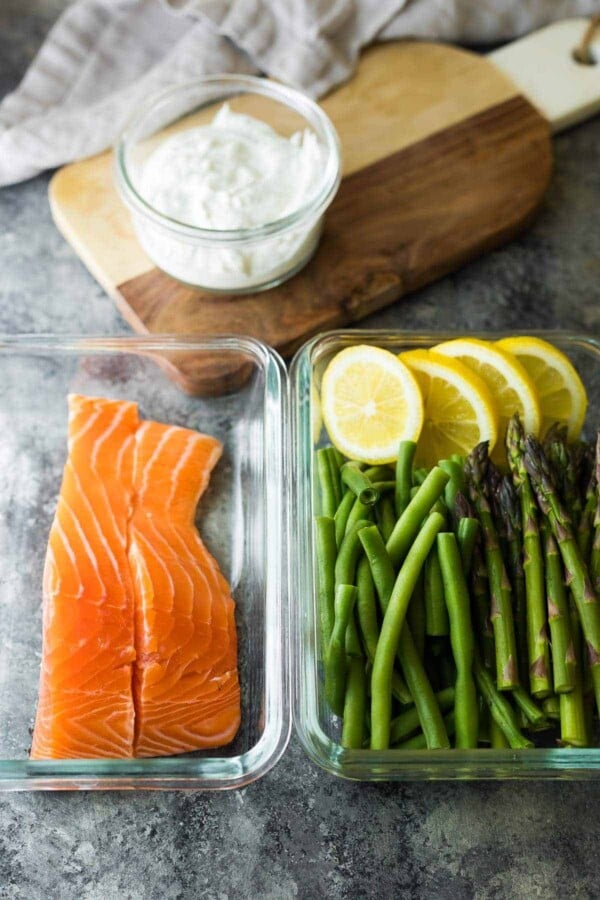 salmon and veggies stored in two meal prep containers for the salmon sheet pan dinner