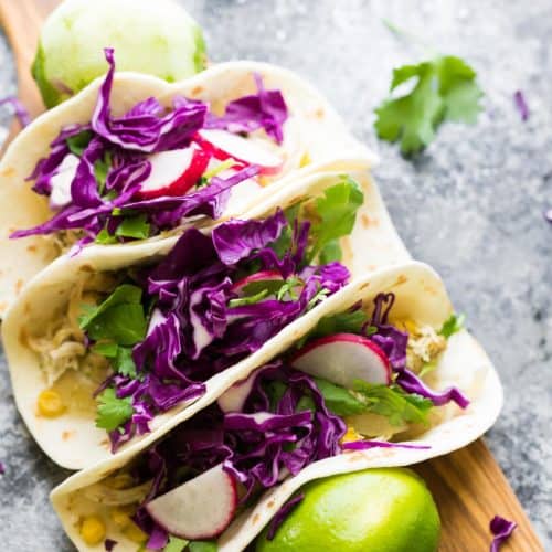three cilantro lime chicken tacos on wood cutting board with fresh limes