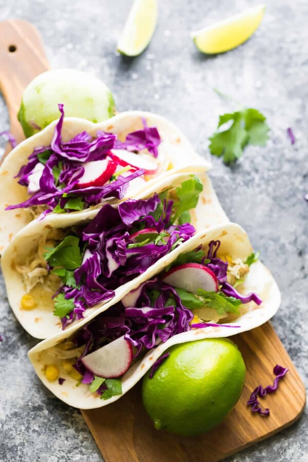 three cilantro lime chicken tacos on wood cutting board with fresh limes
