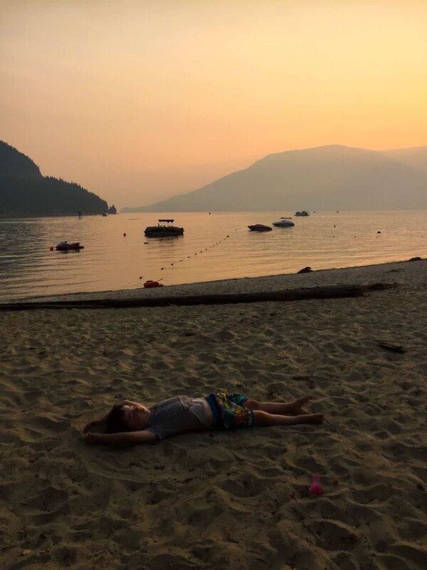 a boy laying in the sand in front of the water