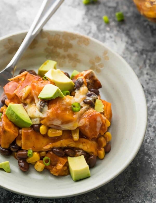 white bowl of butternut squash enchilada casserole and avocado chunks