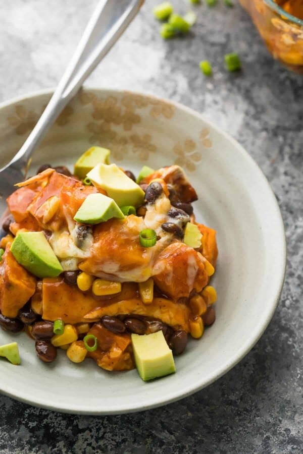 white bowl of butternut squash enchilada casserole and avocado chunks