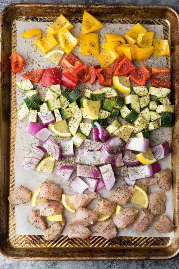 peppers, zucchini, red onion, lemon, chicken with seasoning on sheet pan before baking