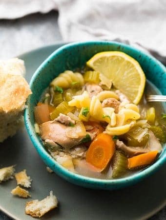 blue bowl with lemon ginger chicken noodle soup with lemon and bread