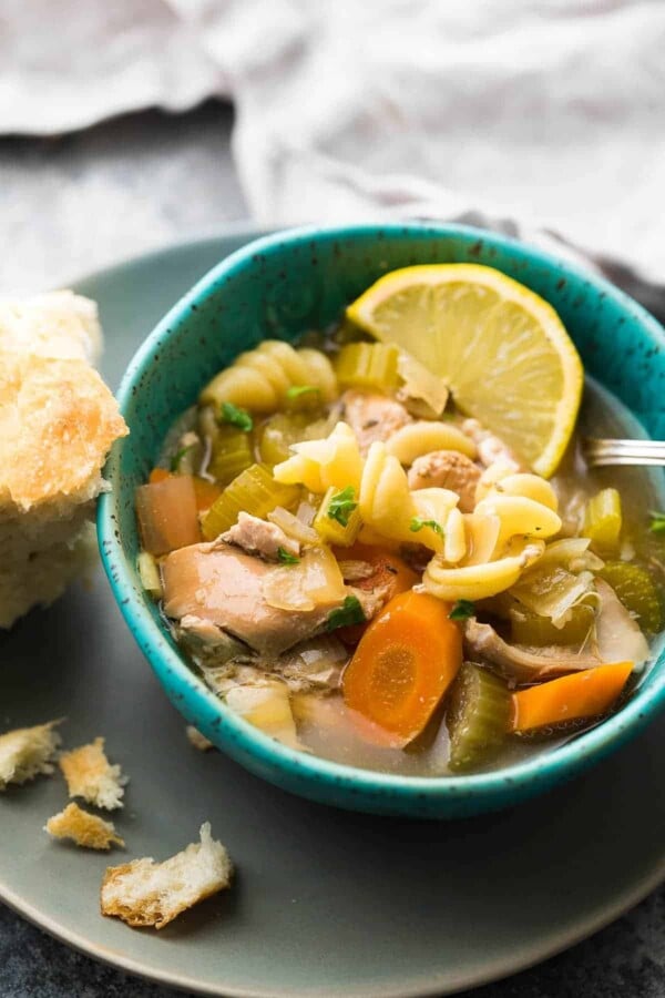 lemon sesame chicken noodle soup in a blue bowl with piece of bread