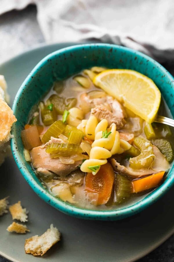 lemon sesame chicken noodle soup in blue bowl with piece of bread