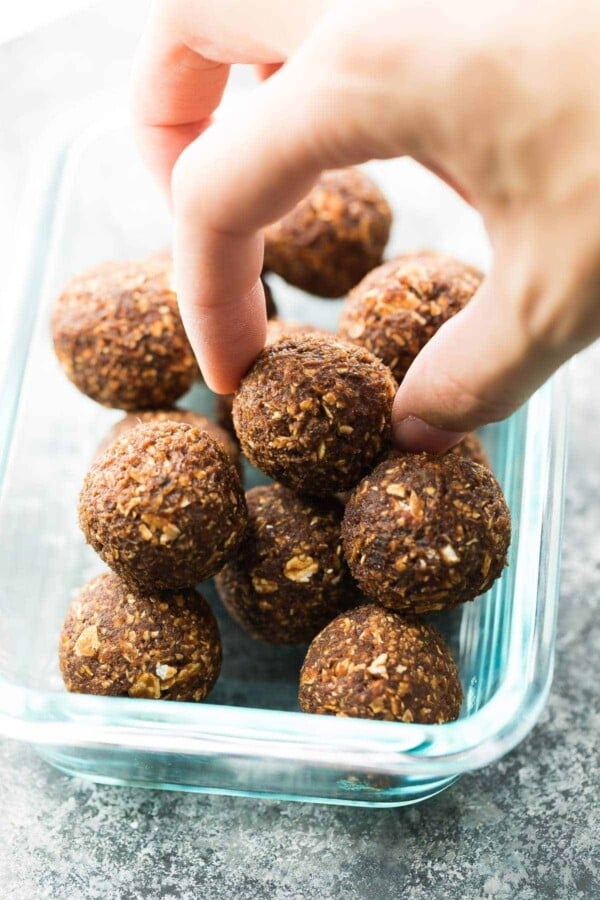 pile of nut free energy bites in a glass container with someone picking one out