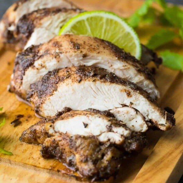 sliced chicken on a wood cutting board with jamaican jerk chicken marinade on it and fresh lime wedges