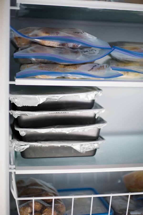 Close up view of four stacked aluminum trays full of freezer lasagna bakes inside freezer