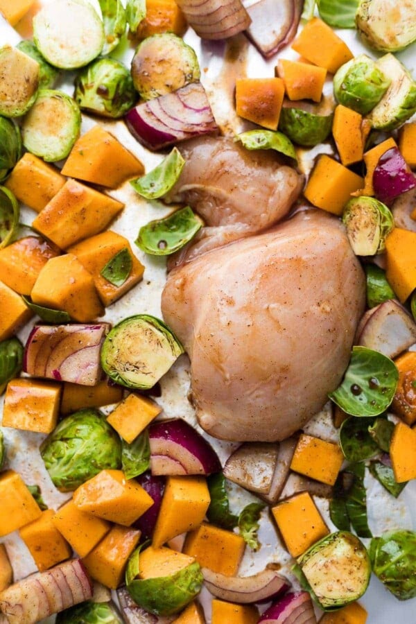 Chopped red onion, brussel sprouts, butternut squash, and raw chicken on sheet pan with balsamic glaze before baking