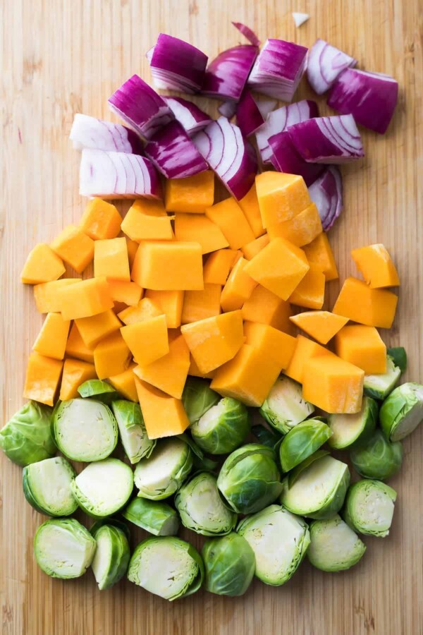 chopped red onions, butternut squash, and brussel sprouts on wood cutting board