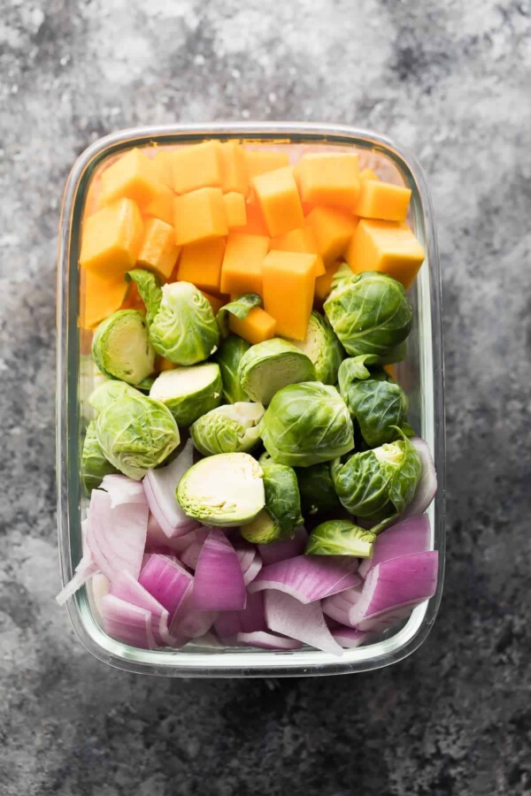 chopped red onions, butternut squash, and brussel sprouts in a glass container