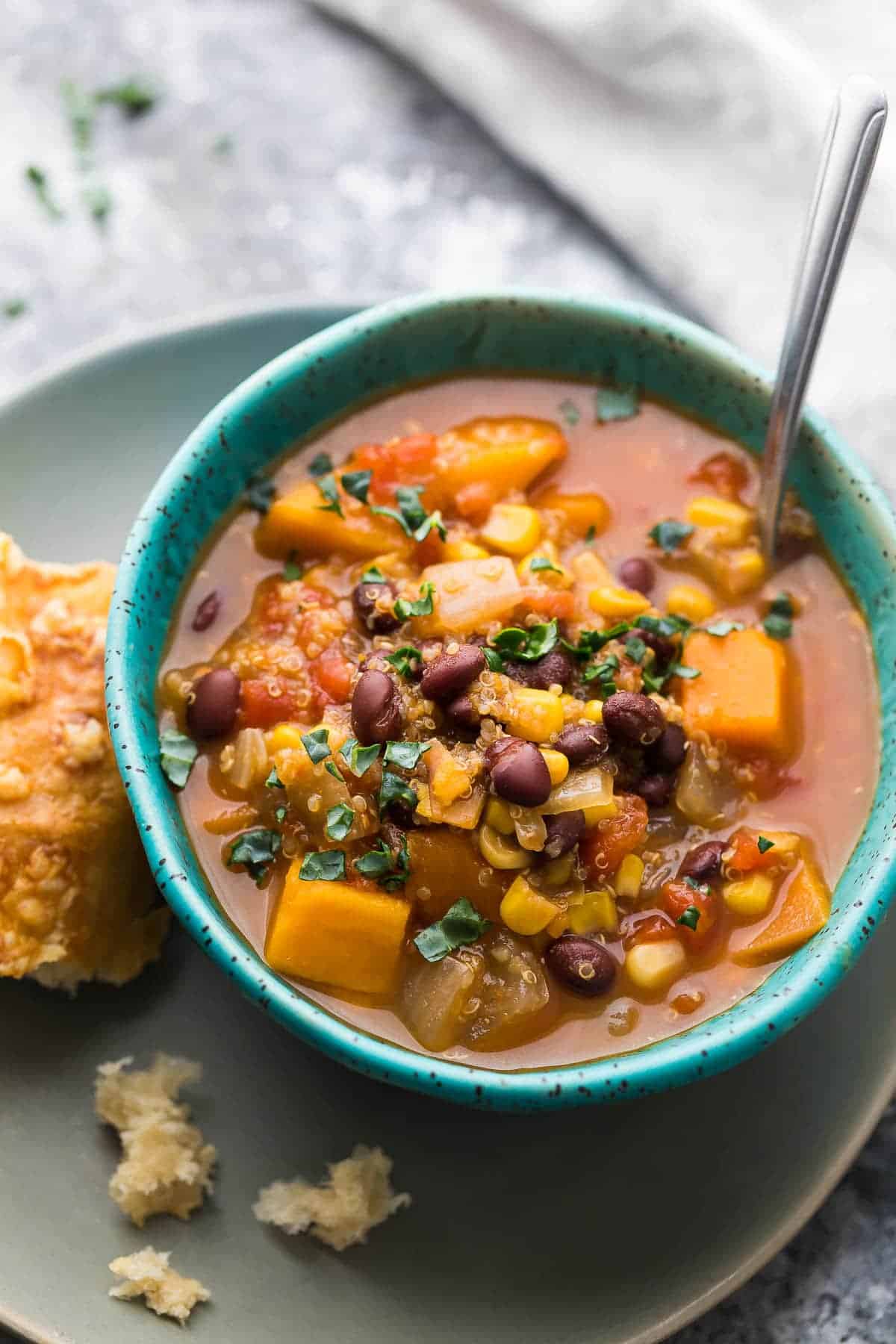 Black bean, quinoa and sweet potato stew in blue bowl with a chunk of bread next to it