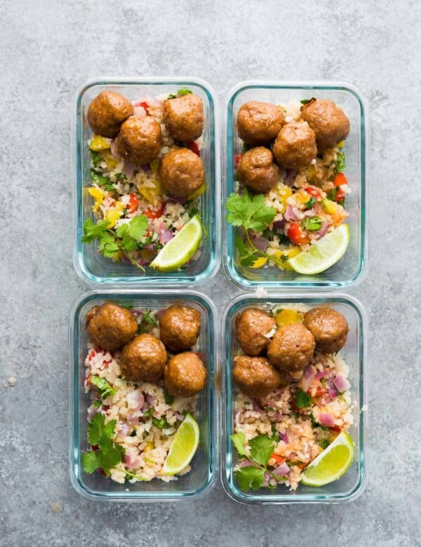 overhead shot of four glass meal prep containers with chipotle honey mealballs, rice and limes