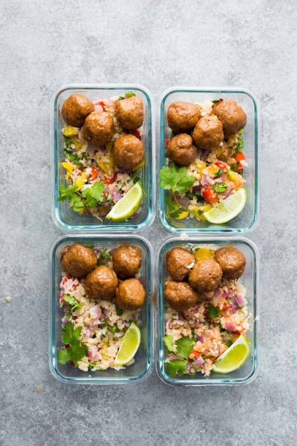 overhead shot of four glass meal prep containers with chipotle honey mealballs, rice and limes