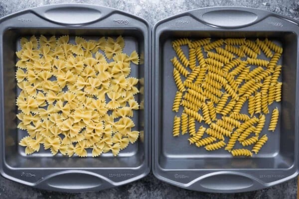 Two baking pans filled with different dried pasta shapes