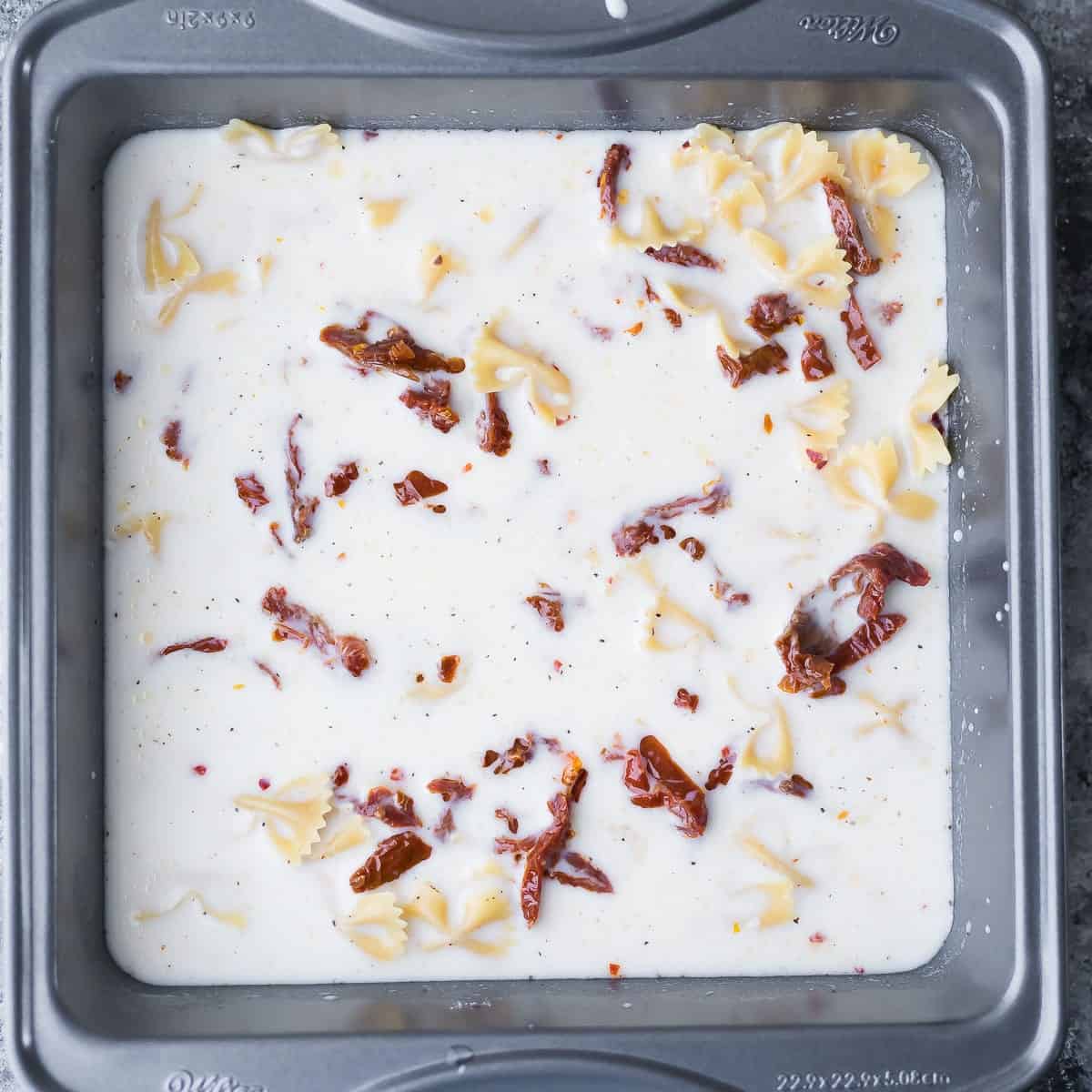 dried pasta, stock, milk, sundried tomatoes and flour in a baking pan before baking