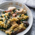 tuscan chicken pasta bake in white bowl with a spoon