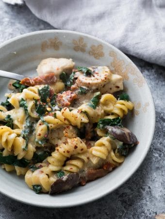 tuscan chicken pasta bake in white bowl with a spoon
