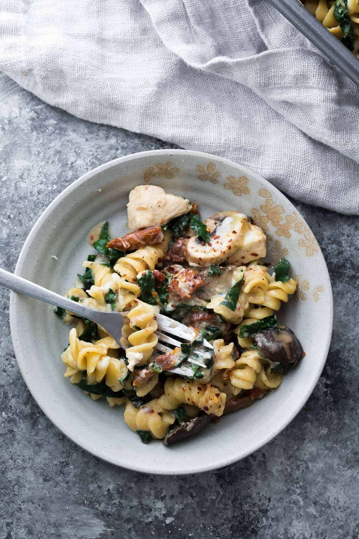 Tuscan chicken pasta bake in a white bowl with a fork