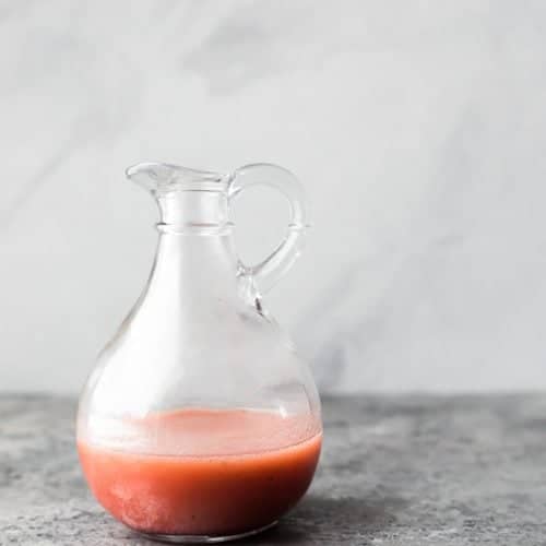 Glass jar with red wine vinaigrette on a gray background