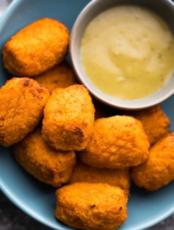 a pile of crispy air fryer sweet potato tots with dipping sauce on blue plate