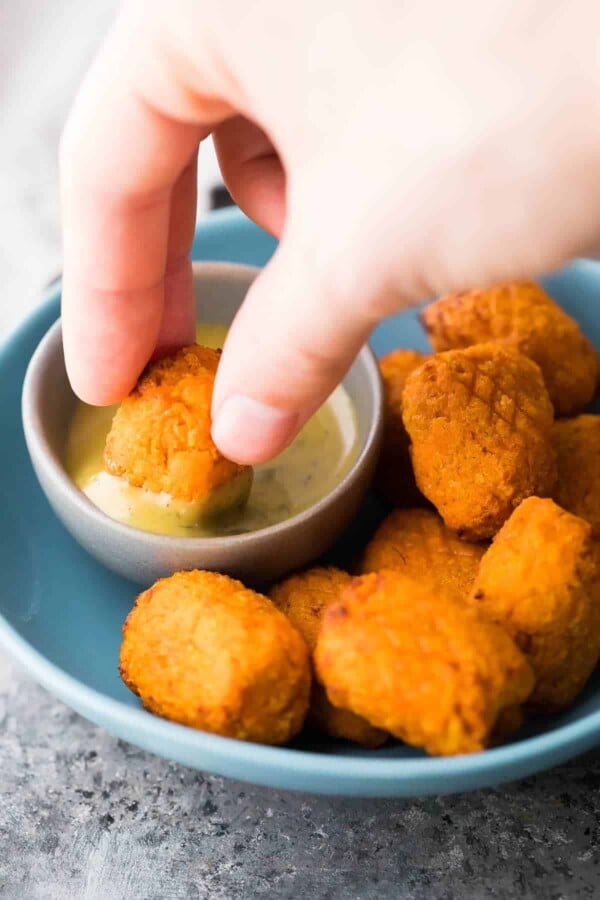 hand dipping Sweet Potato Tots into dipping sauce in blue bowl