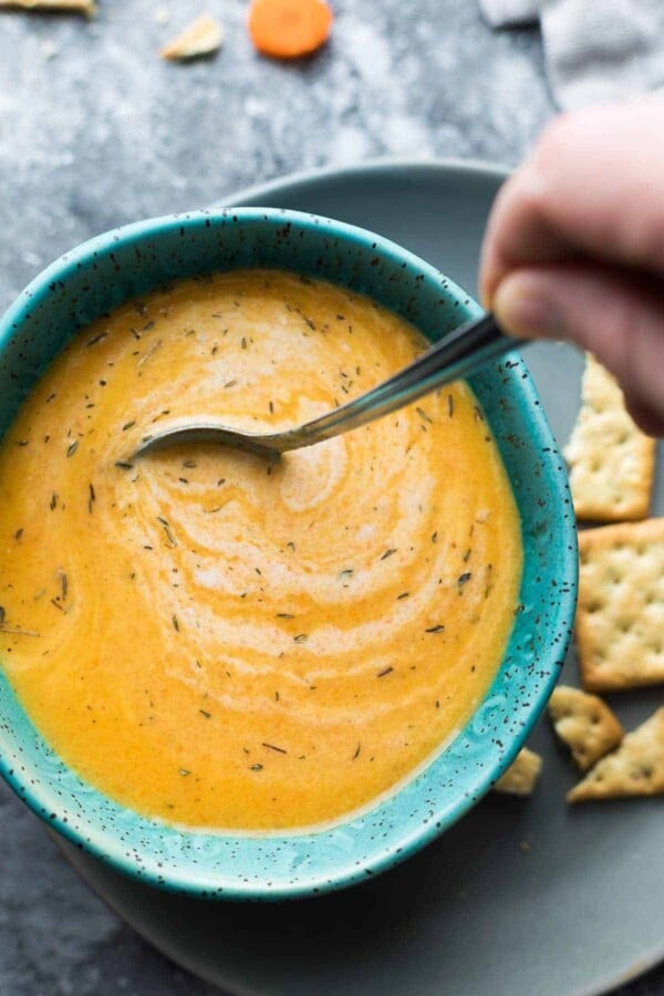 Overhead shot of carrot ginger soup in a blue bowl with a spoon stirring it