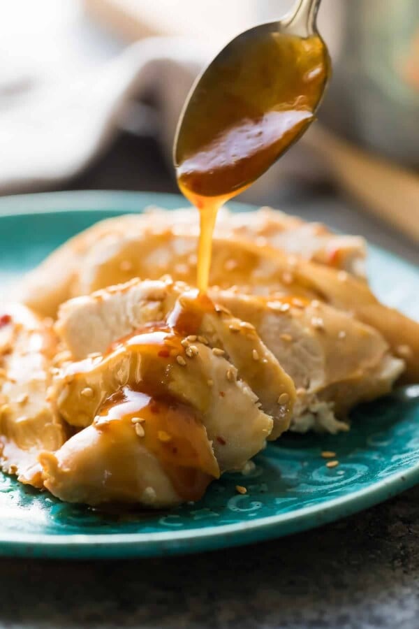 spoon pouring honey sesame glaze over sliced chicken breast on blue plate