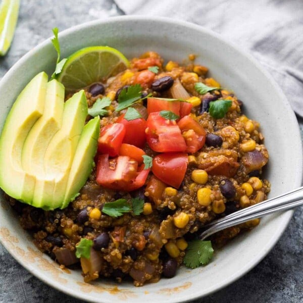 Quinoa Enchilada Casserole in a white bowl with avocado slices, tomatoes, lime wedges, and cilantro