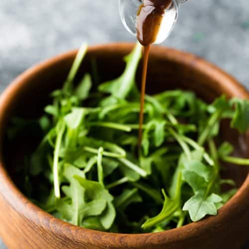 wooden bowl of salad leaves with balsamic vinaigrette being drizzled on top