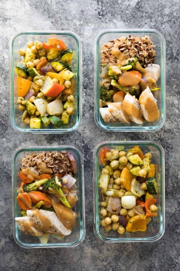 overhead shot of four glass containers filled with pesto chickpea pitas and thai chicken lunch bowls