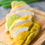 Sliced curry yogurt chicken on a wood cutting board with lime slice