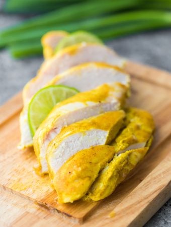 Sliced curry yogurt chicken on a wood cutting board with lime slice