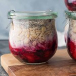 Glass jar of fruit on the bottom overnight oats sitting on wood cutting board