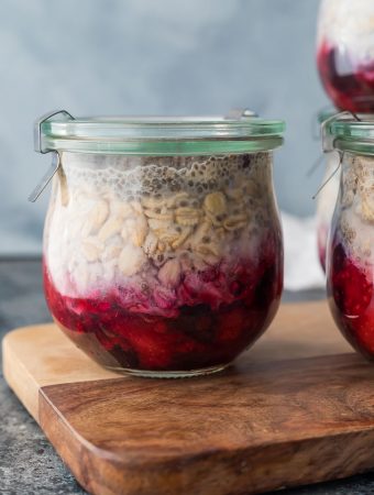 Glass jar of fruit on the bottom overnight oats sitting on wood cutting board