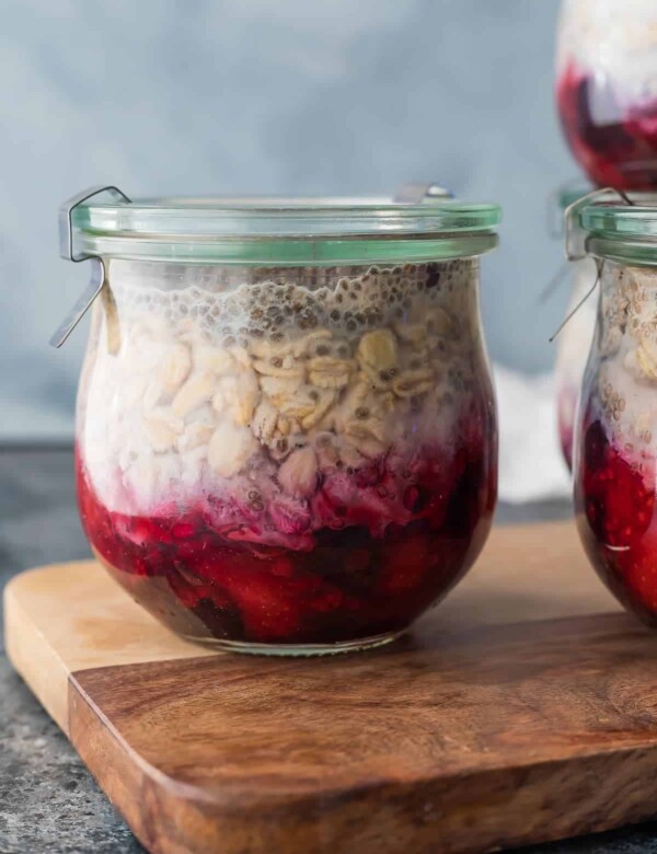 Glass jar of fruit on the bottom overnight oats sitting on wood cutting board