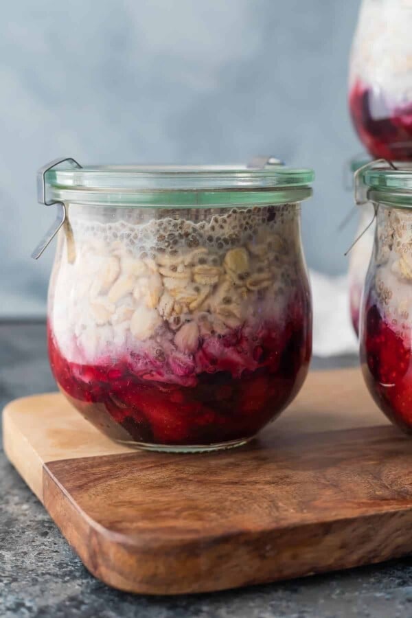 Glass jar of fruit on the bottom overnight oats sitting on wood cutting board