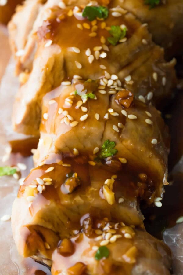 close up overhead view of sliced up instant pot pork tenderloin sprinkled with sesame seeds and drizzled with a sauce
