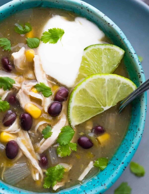 close up shot of chicken chile verde soup with lime wedges and sour cream