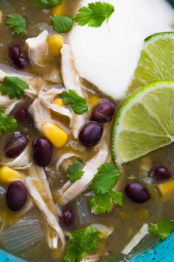 close up shot of Chicken Chile Verde Soup with lime wedges, cream, and cilantro