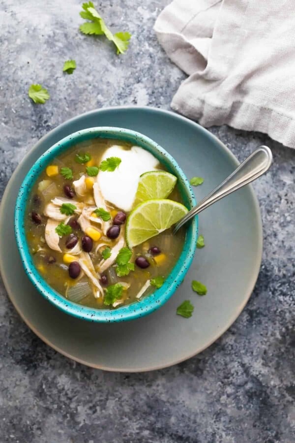 overhead shot of chicken chile verde soup in blue bowl with spoon on gray counter