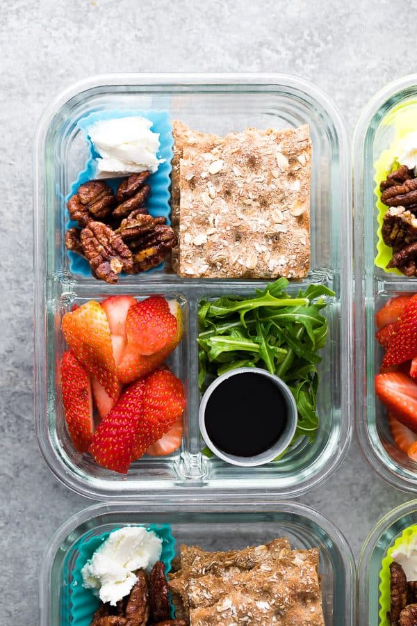overhead shot of spring strawberry bento box with nuts crackers strawberries and salad in glass meal prep container