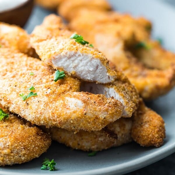 Crispy chicken tenders piled on a plate with fresh parsley
