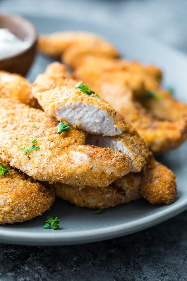 Crispy chicken tenders piled on a plate with fresh parsley